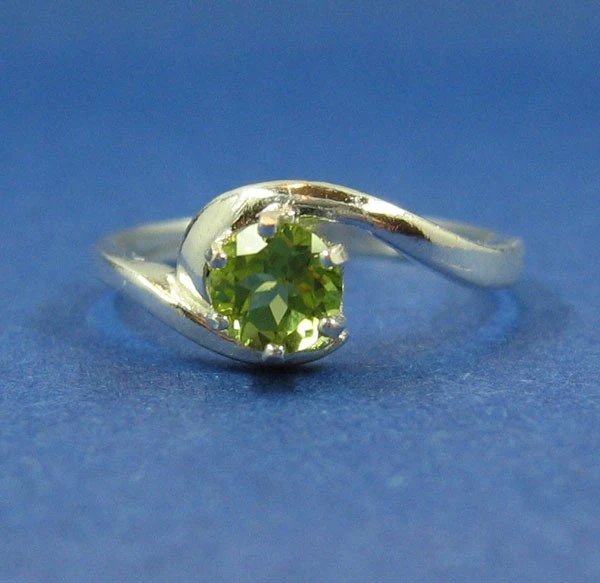 Silberfarbener Solitärring mit grünem Peridot auf blauem Untergrund
